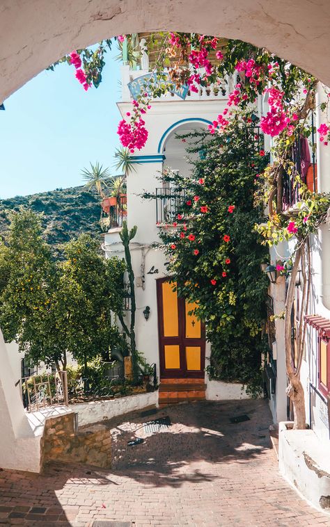 A white house with blue trims and a yellow and brown door, covered in Bougainvillea and Hibiscus flowers framed by a white arch in Mojácar Old Town, Spain. Andalusia, Spain Aesthetics, Spain Bucket List, Spain Aesthetic, Spain Travel Guide, Europe Aesthetic, Europe Summer, Spain And Portugal, Beautiful Places To Travel