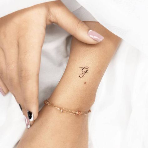 Minimalist letter "G" tattoo on the wrist. Minimalistic Initial Tattoo, Star Tattoos With Initials, G Letter Design Tattoo, G And S Tattoo, Lowercase Cursive G Tattoo, Heart With A G Tattoo, G Wrist Tattoo, Small Letter G Tattoo, Small Letter Tattoos For Women