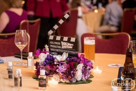 Movie clacker surrounded by purple floral as a reception table centerpiece for a movie wedding theme Wedding Movie Night, Nerdy Centerpieces Wedding, Friends Themed Table, Movie Theme Wedding Ideas, Movie Wedding Ideas, Movie Wedding Theme, Film Theme Wedding, Royal Pacific Resort Orlando, Cinema Themed Wedding