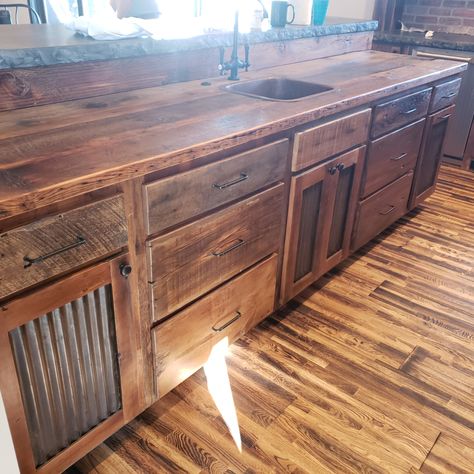 Kitchen of your dreams? Ours too! Check out the live edge concrete, corrugated tin in the doors, and open shelving under the cabinets. This is a show stopper. Custom build just for this space. Come design your dream kitchen with us! 
#Reclaim Renew #customkitchen #kitchen #eat #custom #custombuild #corrugatedtin #barnwood #rustic #farmhouse #style Kitchen Pallet Cabinets, Rustic Cabin Kitchens Open Shelves, Under Counter Cabinet Ideas, Rustic Cabinets Farmhouse Style, Farmhouse Kitchen Open Cabinets, Rustic Kitchen Cabinets Diy, Rustic Farmhouse Cabinets, Pallet Kitchen Cabinets Farmhouse Style, Rustic Cabinets Kitchen Farmhouse Style