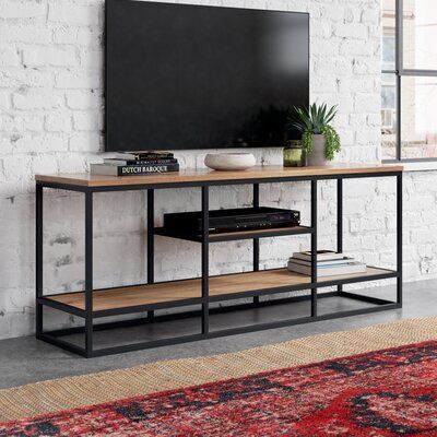 This versatile TV stand features an open, mixed-material design that brings a rustic look to your living room or bedroom. It's made from solid mango wood with a natural brown finish, and it's built on a sleek black metal frame that complements your industrial decor. This rectangular piece measures 63" wide, giving you enough space to display books, organizational baskets, and DVDs on the bottom shelf. The small middle shelf is just right for your cable box or game console. We also love that the Modern Industrial Tv Stand, Black Metal And Wood Decor, Home Decor Ideas Men, Black Tv Cabinet, Industrial Tv Stand, Apartment Stuff, Display Books, Wood Interior Design, Cable Box