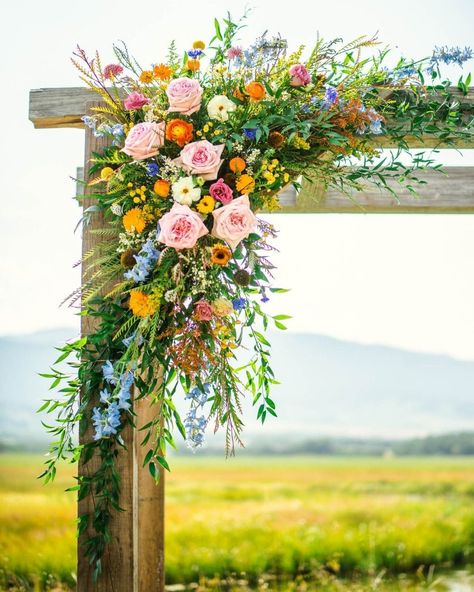 Beartooth Floral and Gifts Wedding Arch Flowers Colorful, Wooden Arbor Wedding Flowers, Wildflower Arch Flowers, Wildflower Arbor Decor, Wedding Arbor Wildflowers, Rustic Wedding Decor Wildflowers, Wildflower Arch Arrangement, Wild Flower Wedding Arbor, Funeral Arrangements Flowers