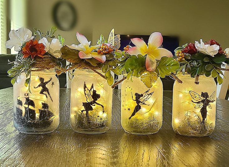 four mason jars with fairy lights and flowers in them on top of a wooden table