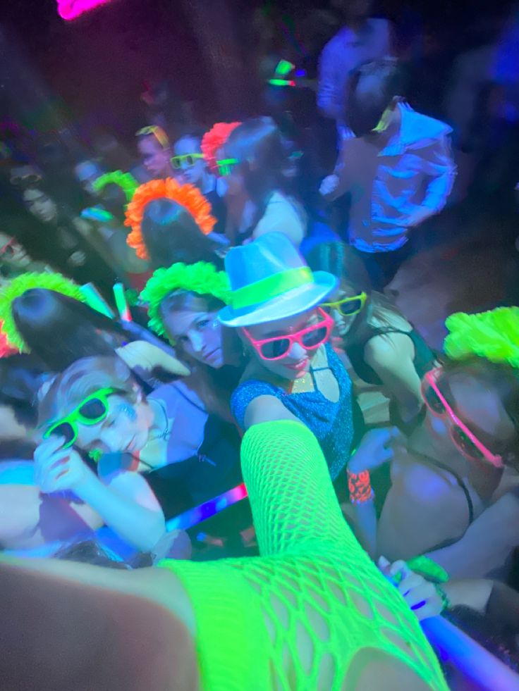 a group of people in neon colored clothing and hats at a party with bright lights