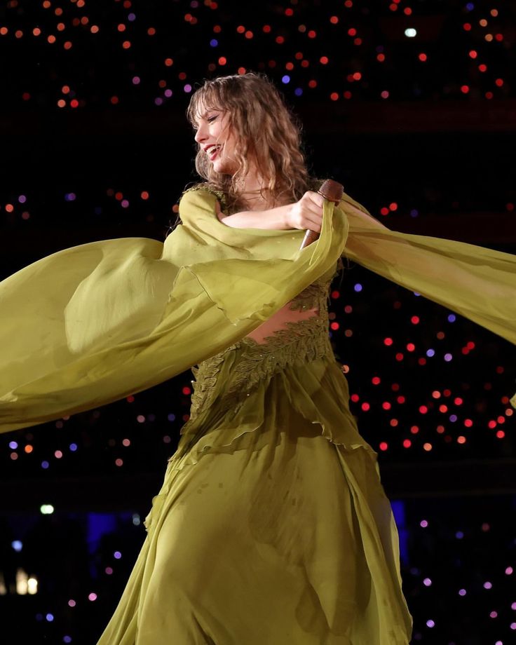 a woman in a yellow dress is dancing on stage with her arms spread out to the side