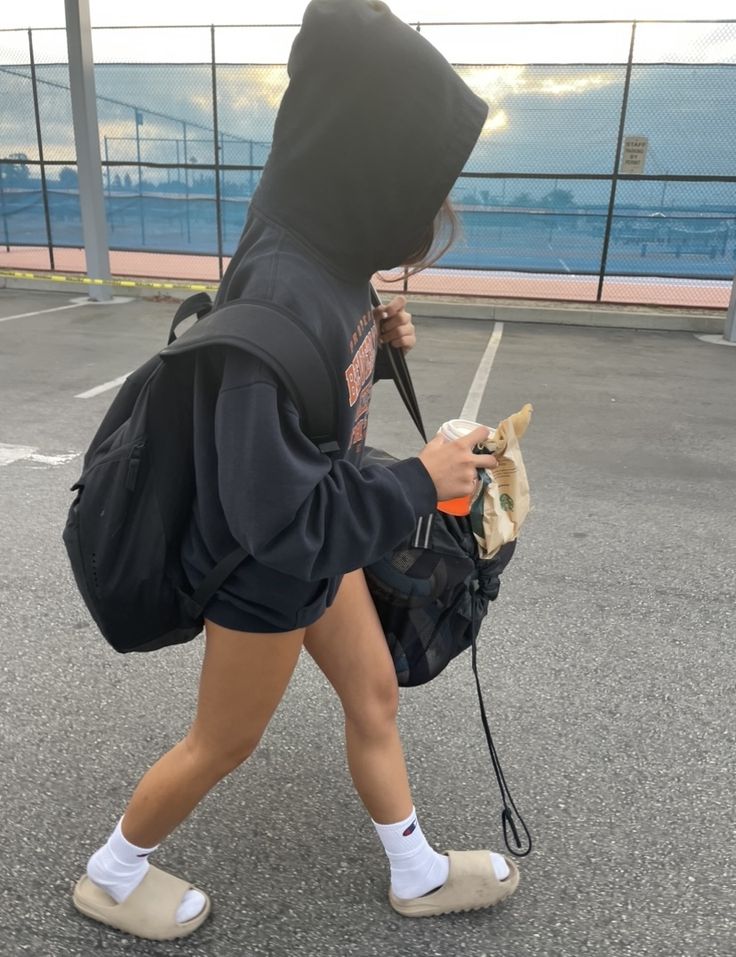 a person in a hoodie walking with a bag and a dog on a leash