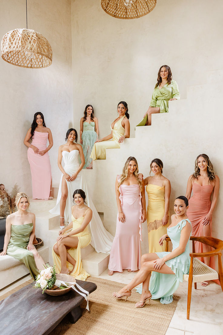 a group of women sitting around each other in different colored dresses on the floor next to a white wall