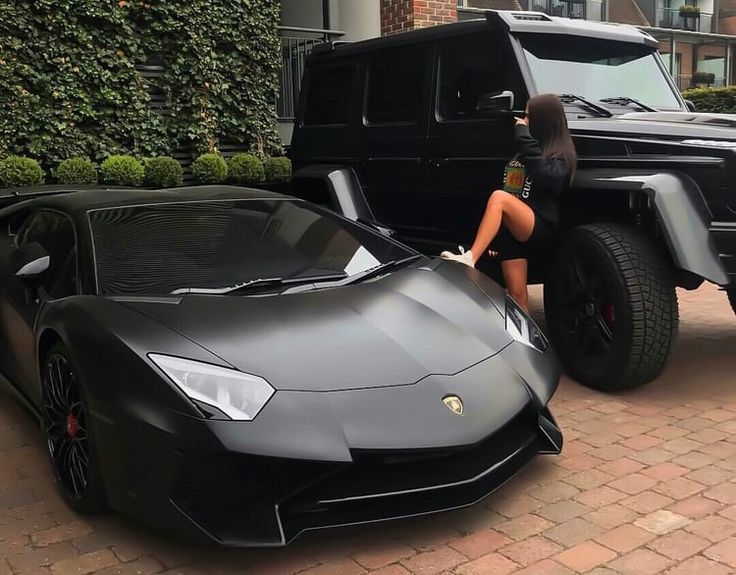 a woman sitting on the hood of a black sports car next to a lambino