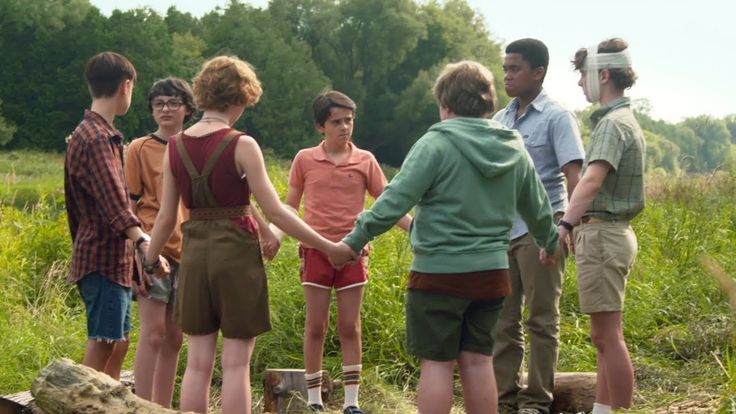 a group of people standing next to each other in a field with trees and grass