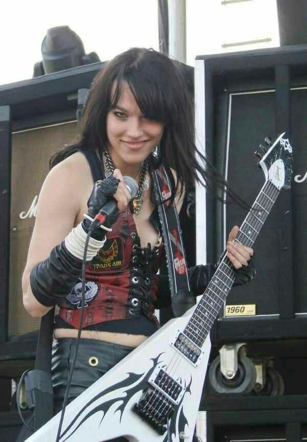 a woman with black hair holding a white guitar in front of an amperator