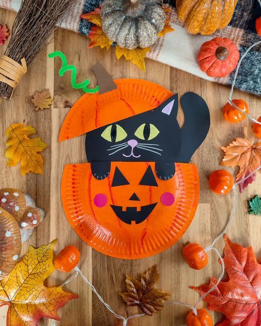 an orange paper plate with a black cat on it, surrounded by fall leaves and pumpkins