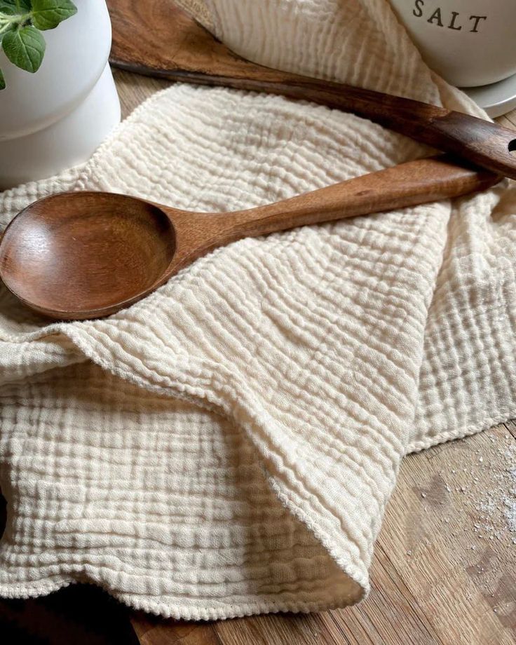 two wooden spoons sitting on top of a towel next to a potted plant