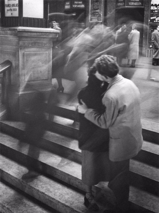 black and white photograph of man sitting on steps with his back to the camera as people pass by