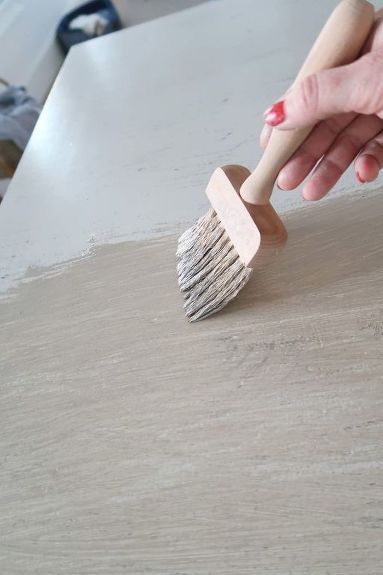 a person holding a brush on top of a wooden table next to a white counter