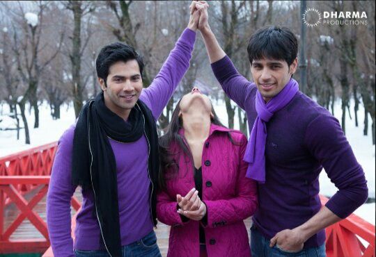 two men and a woman standing together in front of a bridge with their hands up