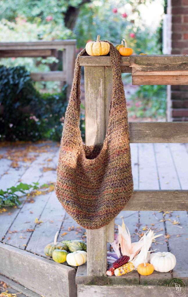 a knitted bag sitting on top of a wooden bench next to pumpkins and gourds