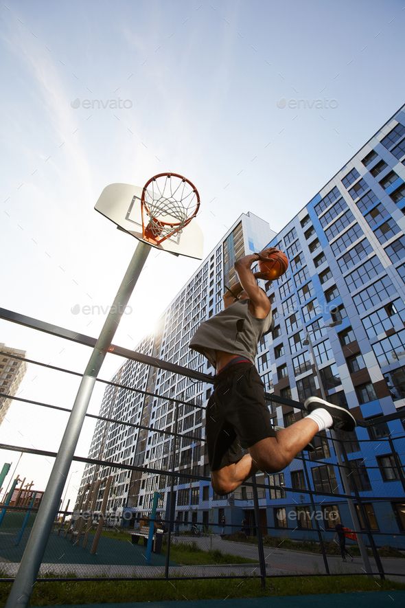 a man jumping up into the air to dunk a basketball in an urban setting