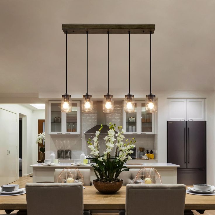 a dining room table with chairs and lights hanging from it's ceiling over the kitchen