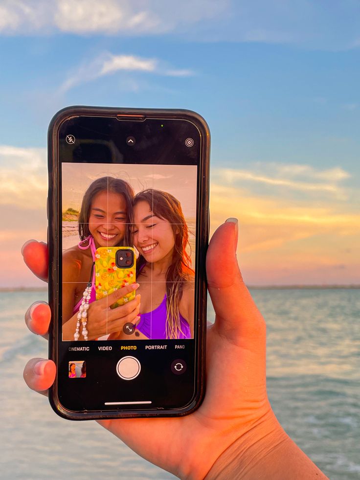 a person holding up a cell phone to take a selfie with the ocean in the background