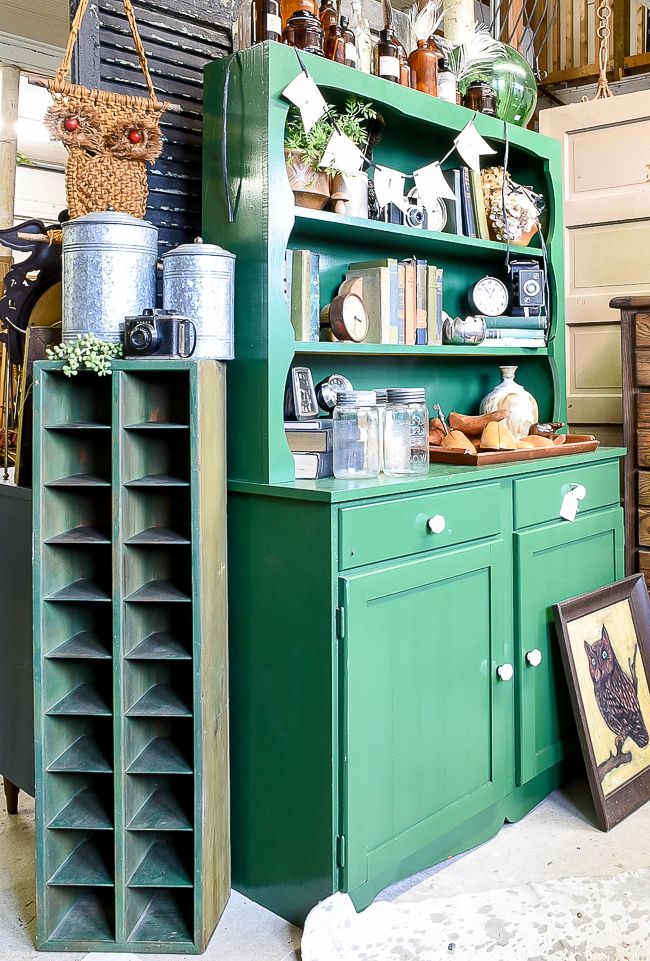 an old fashioned green cabinet with lots of items on the top shelf and bottom shelf