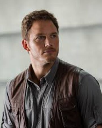 a man wearing a brown leather vest standing in front of a gray wall and looking at the camera