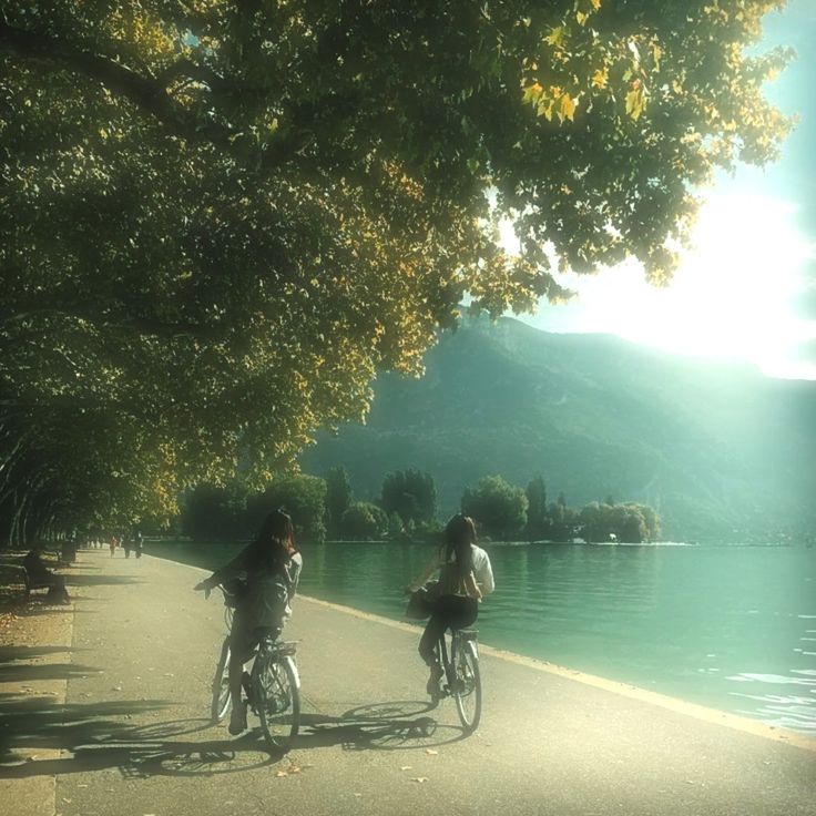 two people riding bikes down a path next to a body of water on a sunny day