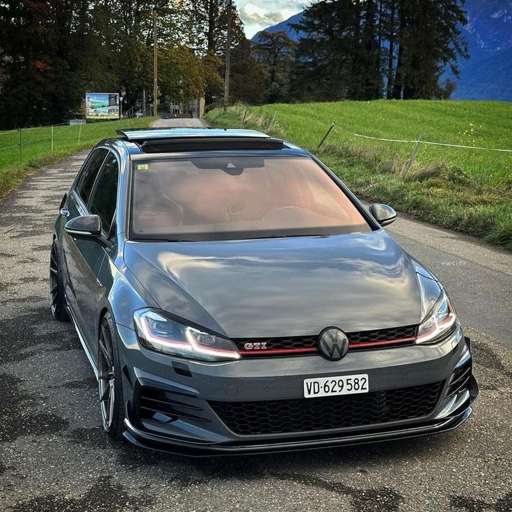 a grey car parked on the side of a road next to a lush green field