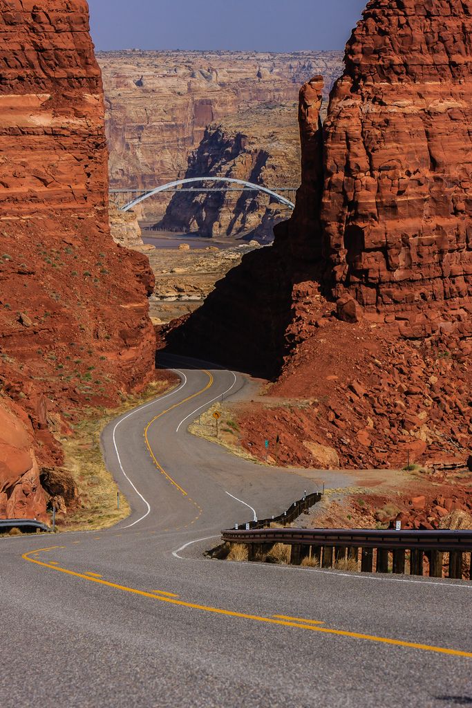 an empty road in the middle of some red rocks with a bridge crossing over it