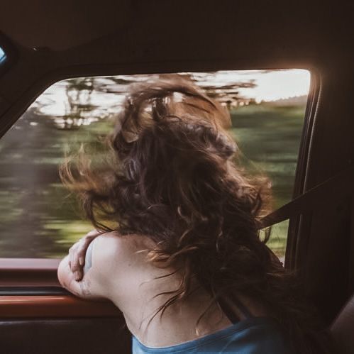 a woman sitting in the back seat of a car looking out the window at trees