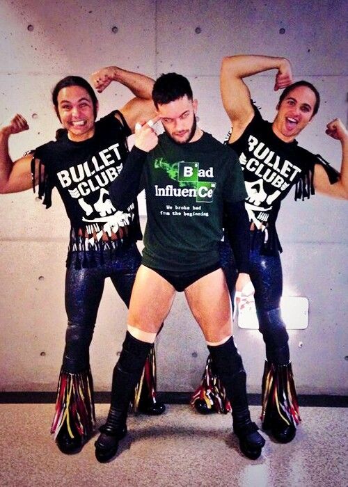 three people wearing boots and t - shirts with their arms around each other while standing in front of a wall