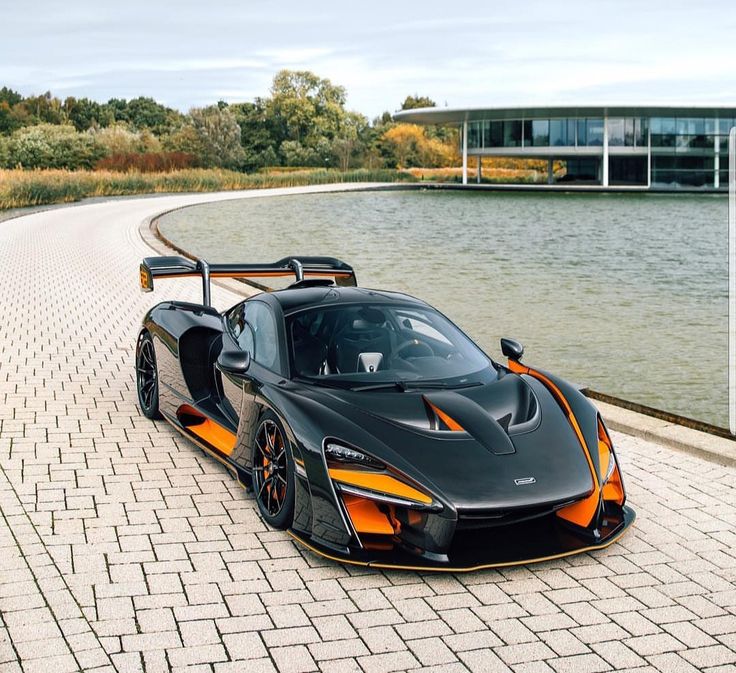 a black and orange sports car parked on the side of a road next to a body of water