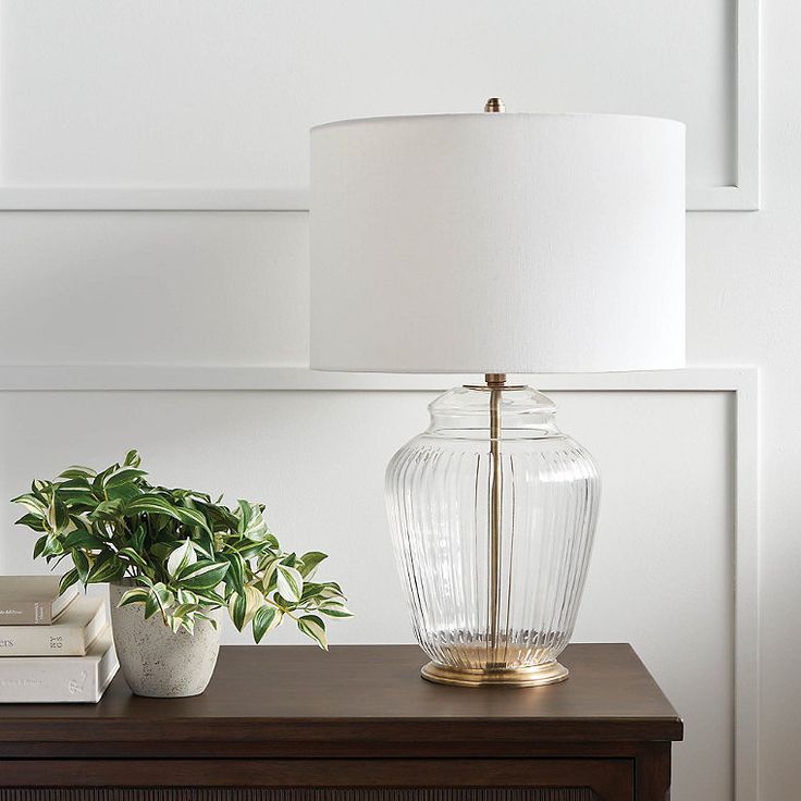 a table with a lamp, potted plant and books on it