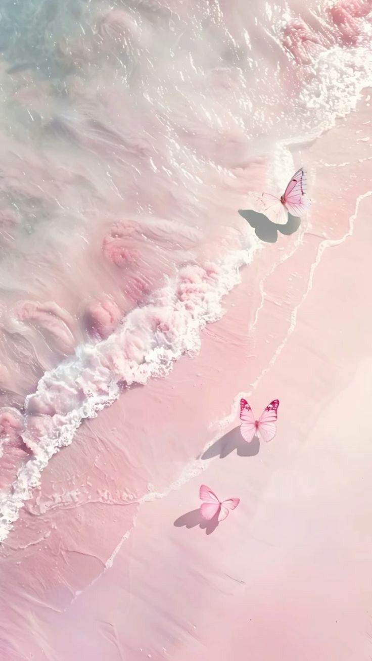 three pink butterflies are flying over the water at the edge of the beach, with waves coming in to shore