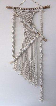 a white wall hanging on the side of a wall next to a wooden stick and yarn