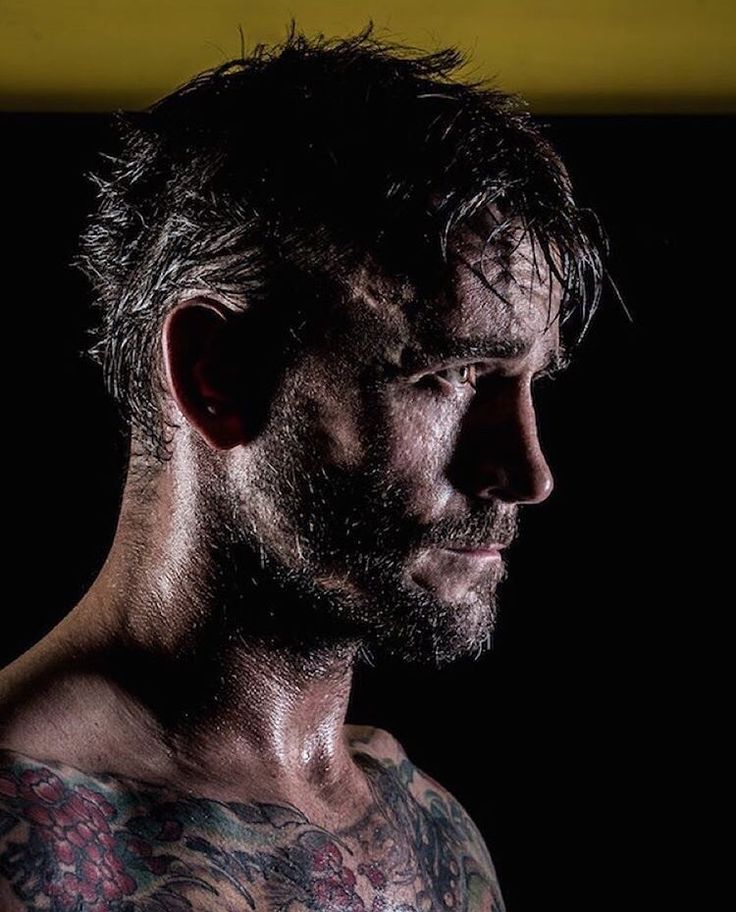 a man with tattoos on his arm and chest looking off to the side in front of a black background