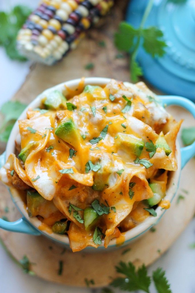 a bowl filled with cheesy pasta and vegetables on top of a wooden cutting board