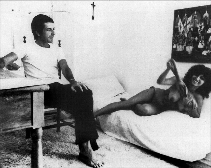 a man and woman sitting on a bed in a room with pictures on the wall