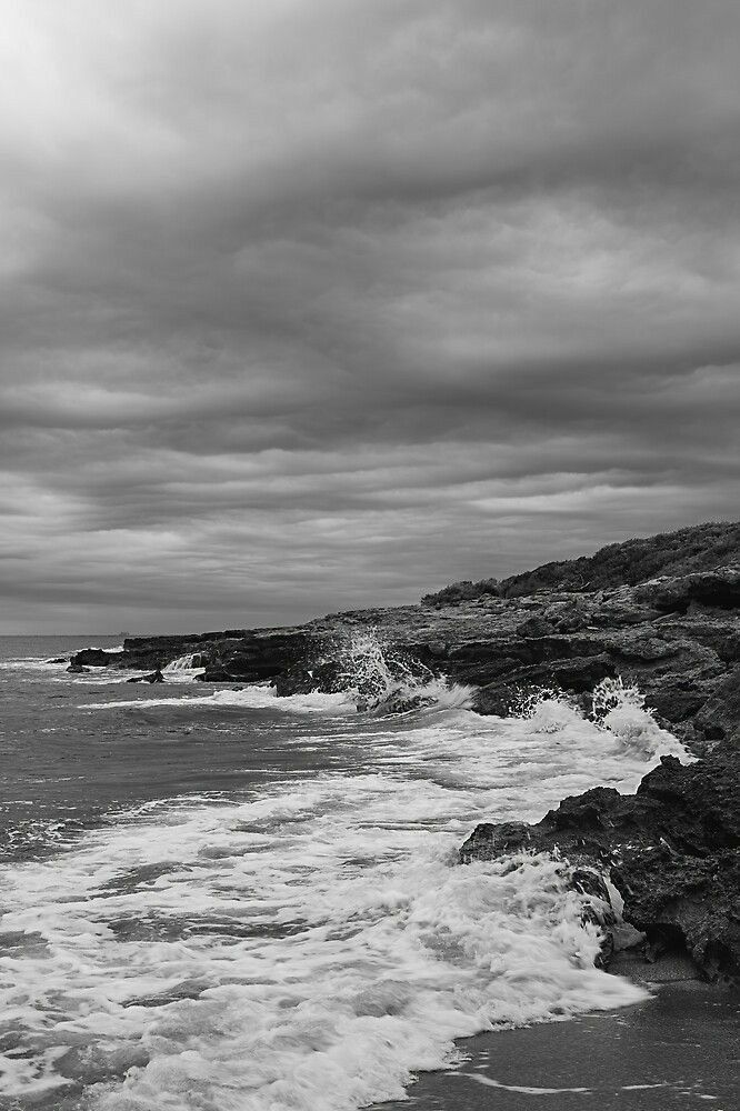 a black and white photo of waves crashing on the rocks by the ocean with an overcast sky