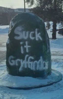 a large rock with writing on it in the middle of snow covered ground next to trees