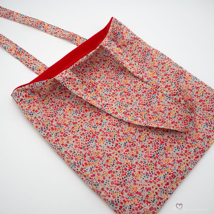an open bag with a red ribbon on the bottom and small flowers all over it