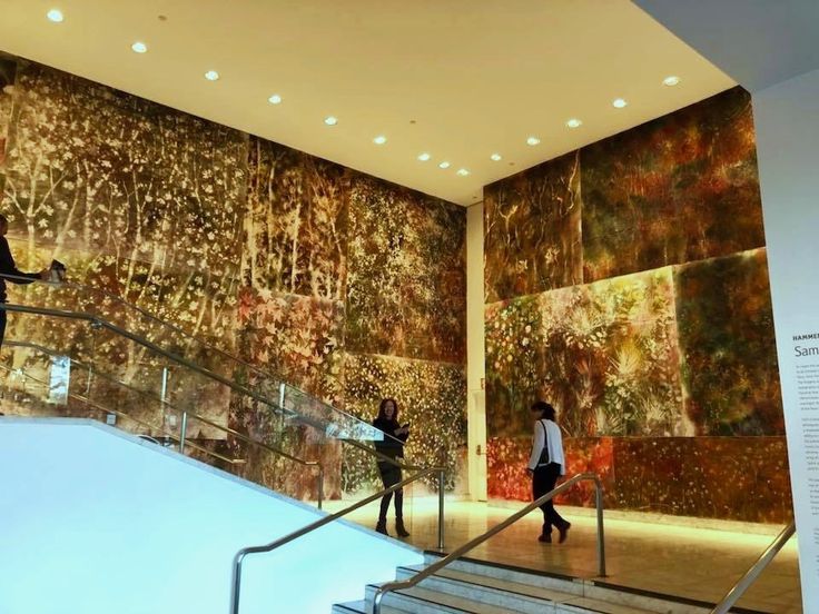 two people walking up and down the stairs in a building with paintings on the walls