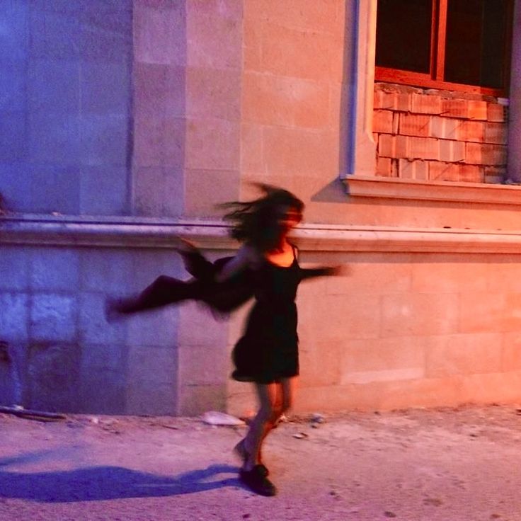 a woman is running down the street in front of a building with her arms spread out