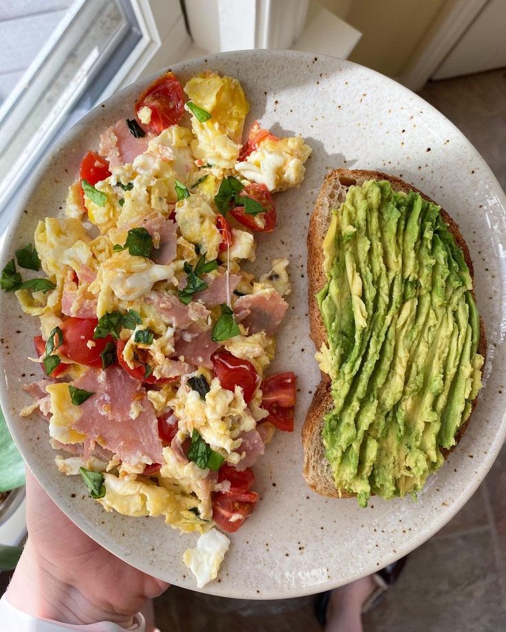 a person holding a plate with an avocado and egg salad on it next to a slice of bread