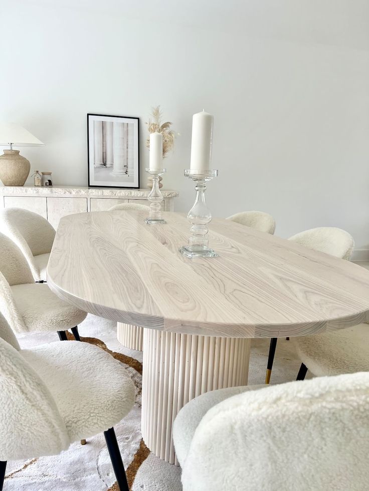 a dining room table with white chairs and a candle on the end shelf in front of it