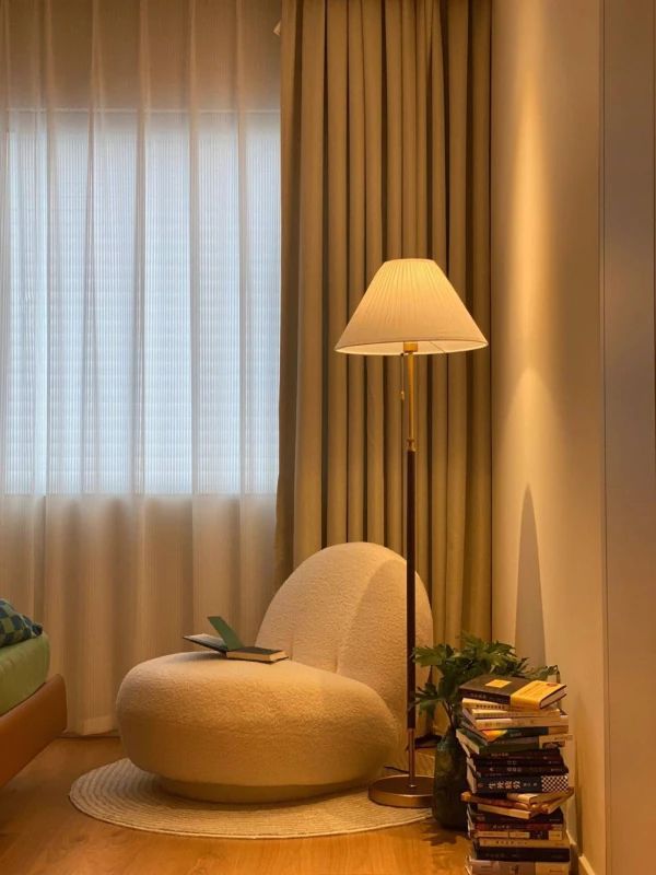 a living room with a lamp, chair and books on the floor in front of a window