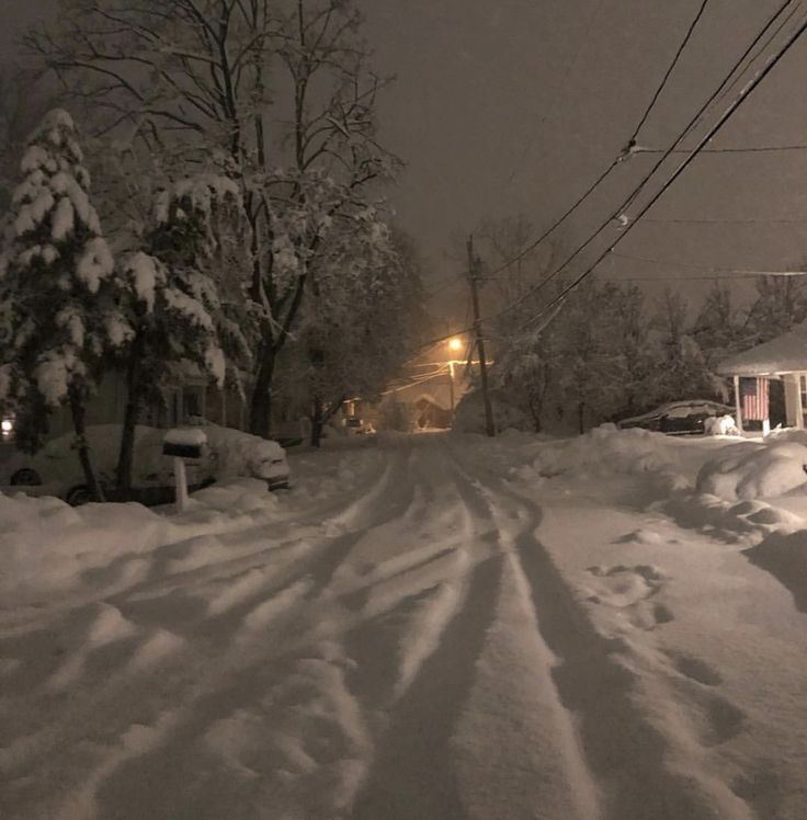 a street covered in snow at night with cars parked on the side and power lines above