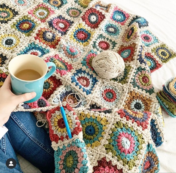 a woman is holding a cup of coffee and crocheted afghan