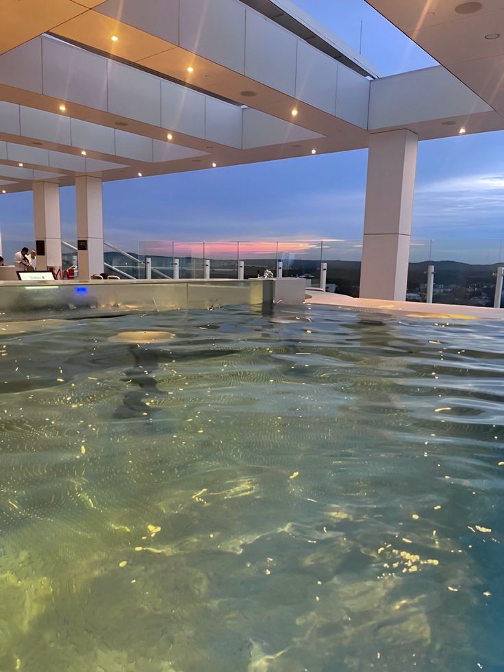 an indoor swimming pool with clear blue water and people sitting on the ledges in the background