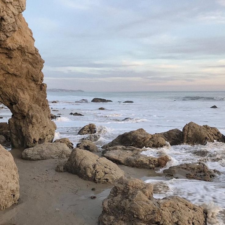 a rock formation on the beach with waves coming in from the ocean and rocks sticking out of the water