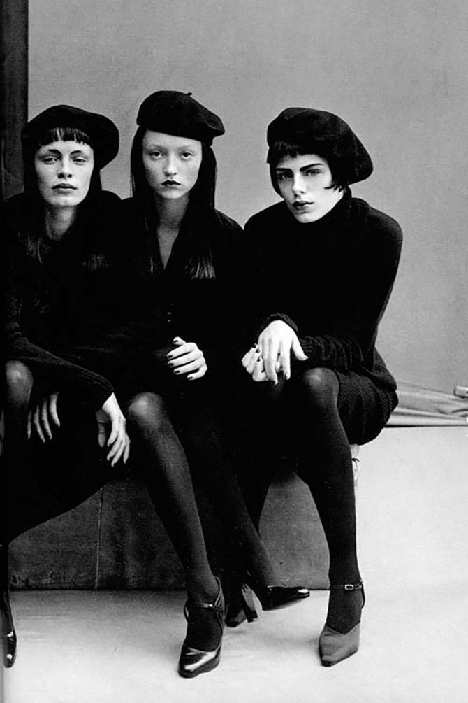 three women sitting next to each other in black outfits and hats, posing for the camera